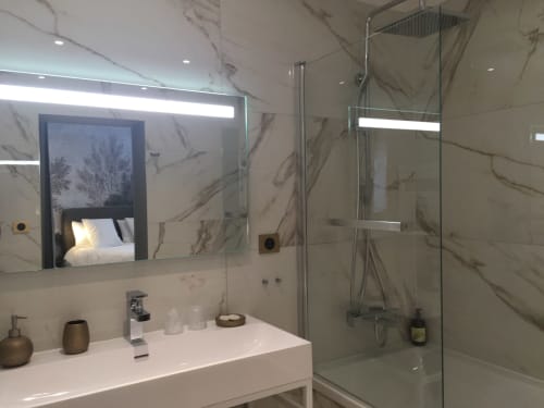 Modern bathroom in Le château d'Hermonville with marble tiles, white sink, large mirror, rainfall shower, and bedroom view