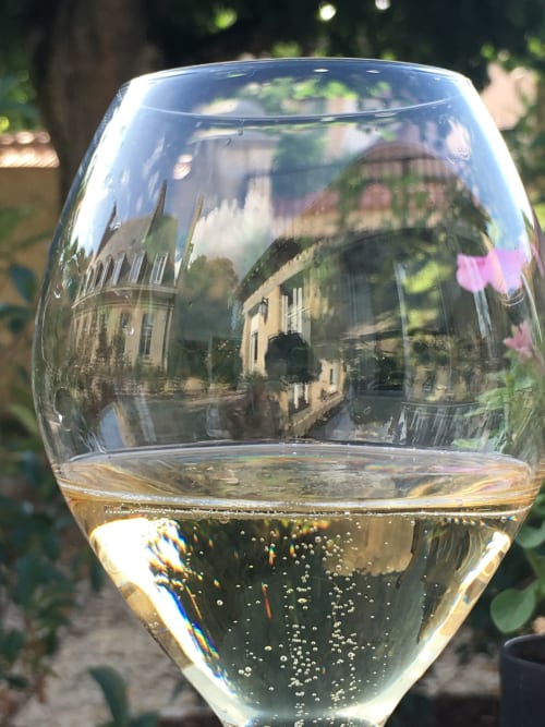 Glass of sparkling wine with European château reflection in garden setting at Le château d'Hermonville boutique hotel
