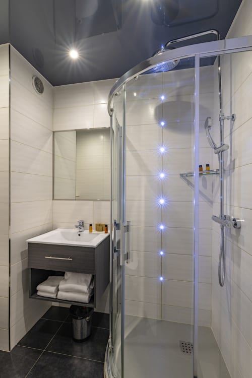 Modern bathroom with illuminated walk-in shower, sink vanity, and heated ceiling at Hotel Residence Europe & Spa, Clichy