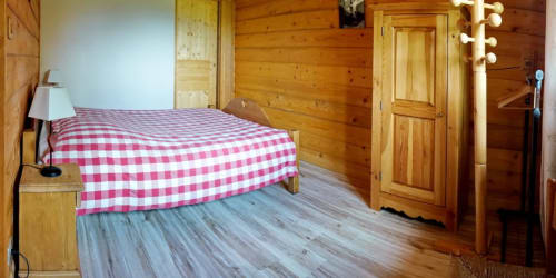Cozy wooden cabin bedroom at Chalet La Louvière with red checkered bedding, wood paneling, and mountain lodge atmosphere in