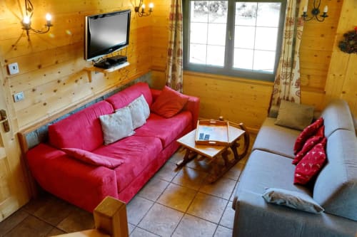 Séjour douillet dans la chambre Grand Loup du Chalet La Louvière avec canapé rouge, fauteuil gris, TV et vue sur les montagnes