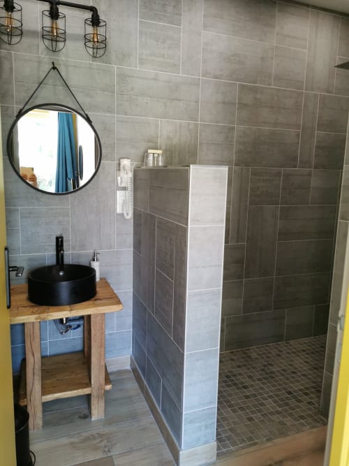 Salle de bain moderne avec vasque noire, miroir rond et douche à l'italienne au gîte La Cour d'Hortense