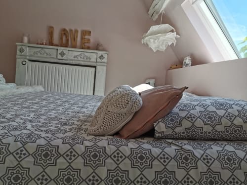 Chambre cosy à La Cour d'Hortense avec parure patterned, coussin marron, jeté tricoté et panneau LOVE au-dessus du radiateur