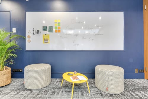 Modern collaborative workspace with whiteboard, two cream poufs, yellow table at Hotel Residence Europe & Spa in Clichy,
