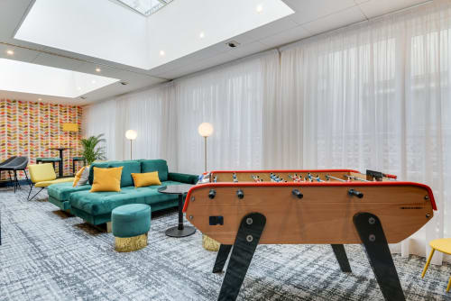 Modern games lounge with foosball table, turquoise sofa, and skylight at Hotel Residence Europe & Spa in Clichy