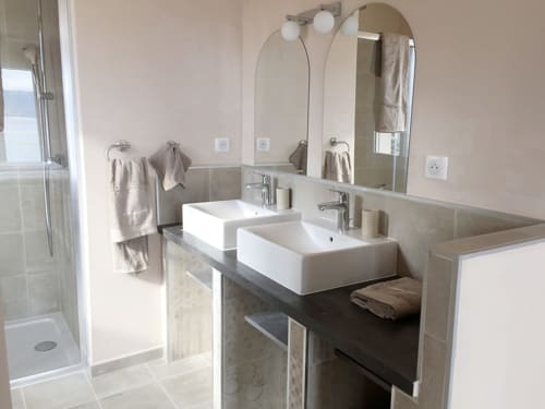 Modern bathroom at Villas Marincelu with dual vessel sinks, arched mirrors, and walk-in shower in Porto Pollo, Corsica.