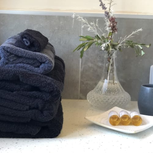 Aménités de salle de bain aux Villas Marincelu : serviettes roulées, fleurs fraiches et savons dorés sur comptoir en marbre