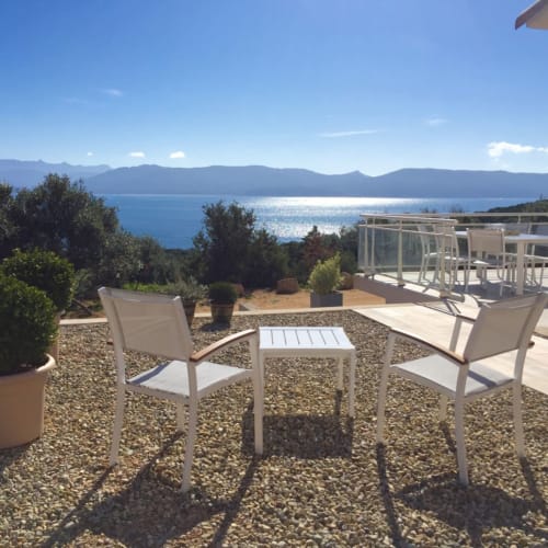 Seaside terrace at Villas Marincelu with white chairs, table, and mountain views overlooking Porto Pollo, Corsica