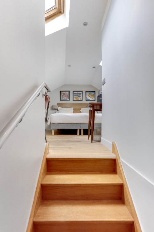 Escalier en bois menant à une chambre Deluxe moderne à l'Hôtel Louvre Richelieu Paris avec murs blancs et puits de lumière