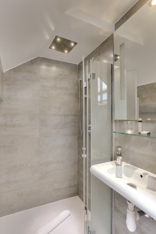 Salle de bain moderne de la chambre Deluxe de l'Hôtel Louvre Richelieu à Paris, avec douche vitrée, lavabo blanc et carrelage beige
