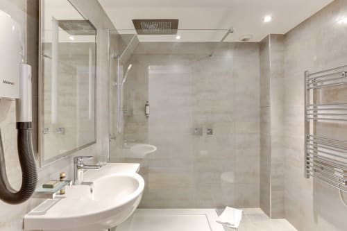 Salle de bains moderne à l'Hôtel Louvre Richelieu Paris avec lavabo blanc, douche spacieuse, sèche-serviettes chauffant et pluie au plafond