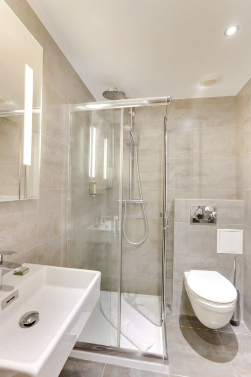 Salle de bain moderne à l'Hôtel Louvre Richelieu Paris avec douche vitrée, lavabo blanc et toilettes murales