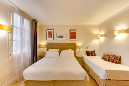 Chambre Triple Comfort de l'Hôtel Louvre Richelieu Paris avec deux lits, éclairage chaleureux et équipements modernes