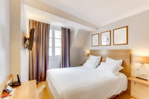 Chambre Double Confort lumineuse à l'Hôtel Louvre Richelieu, Paris avec lit en bois, draps blancs, bureau et rideaux rayés