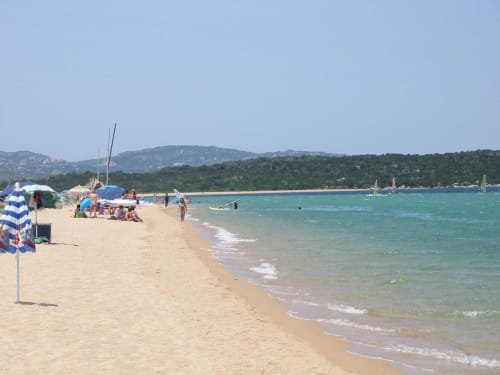 Plage de sable aux Villas Marincelu à Porto Pollo, Corse avec eaux turquoise, voiliers et transats ombragés