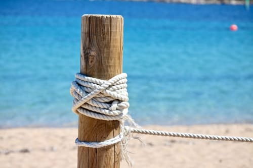 Poteau d'amarrage en bois avec cordage à la plage de Villas Marincelu à Porto Pollo, Corse, surplombant les eaux turquoise de la Méditerranée