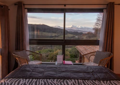 Bedroom at Belloréade B&B in Belloc with mountain view, bed, wicker chairs, and snow-capped peaks visible through large