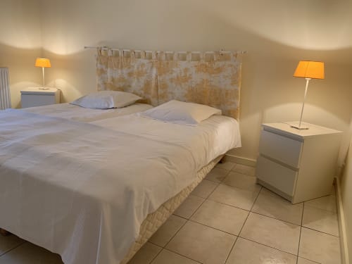 Helles Schlafzimmer im Gästehaus La Croix De La Jarrie in Châtres mit cremefarbener Bettwäsche, gemustertem Kopfteil und warmem Lampenlicht