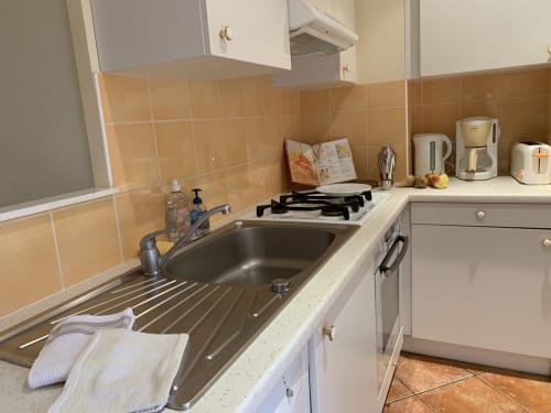 Ausgestattete Küche der Wohnung La Croix De La Jarrie mit Herd, Spüle, weißen Schränken, Fliesenspiegel in Pfirsichfarbe und Arbeitsplatte