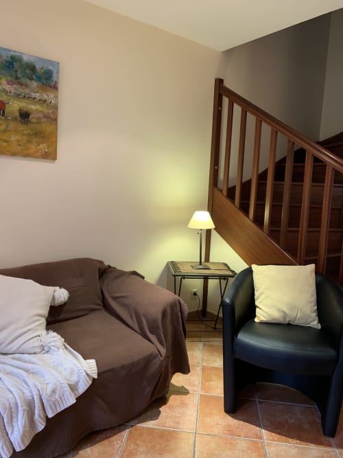 Gemütliches Schlafzimmer im Gästehaus La Croix De La Jarrie mit braunem Sofa, dunklem Sessel, hölzerner Treppe und Tischleuchte in Châtres