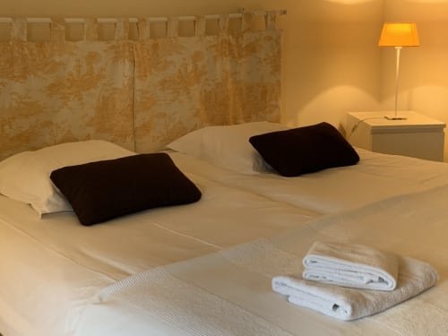 Gemütliches Schlafzimmer im La Croix De La Jarrie B&B in Châtres mit Einzelbetten, schwarzen Kissen, weißen Handtüchern und warmem Licht