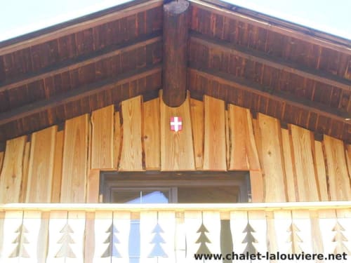 Houten chaletgevel met Zwitsers kruis en decoratieve uitgesneden bomen bij Chalet La Louvière, Fontcouverte-La Toussuire