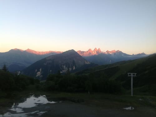 Alpien zonsopgangzicht vanuit Chalet La Louvière in La Toussuire, Frankrijk, met beboste hellingen en weiden.