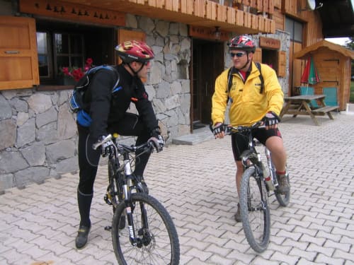 Twee fietsers met helmen buiten Chalet La Louvière in Fontcouverte-La Toussuire, Frankrijk, klaar voor een mountainbike-avontuur.