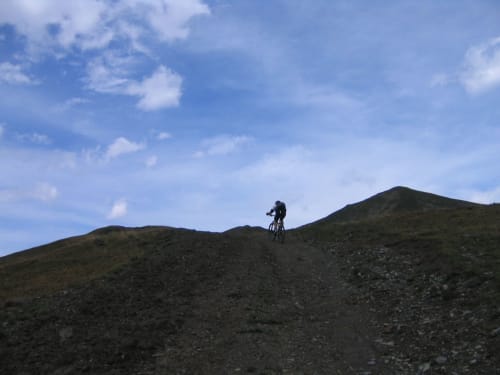 Een mountainbiker rijdt over een rotsachtig pad bij La Toussuire onder blauwe lucht