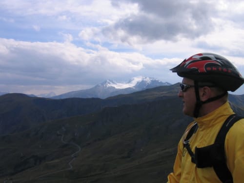 Wielrenner in geel jasje kijkt uit over sneeuwberggen in de Alpen nabij La Toussuire, Fontcouverte