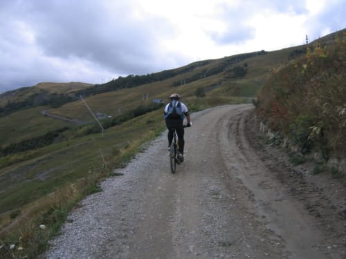 Mountainbiker op grindpad nabij La Toussuire, Fontcouverte. Groene heuvels en alpien landschap.