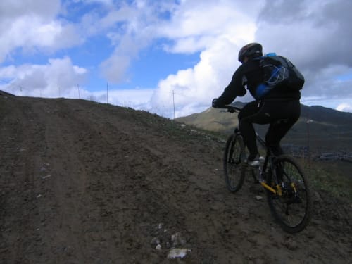 Mountainbiker rijdt op een stoffig pad in de buurt van Fontcouverte-La Toussuire met alpine pieken en blauwe lucht