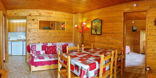 Cozy wooden chalet interior at La Louvière with red patterned beds, dining table, and kitchenette in Fontcouverte-La