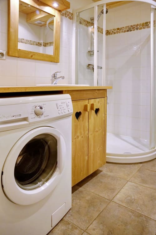 Modern bathroom with washing machine at Chalet La Louvière, La Toussuire, featuring white tiles and wooden vanity with shower