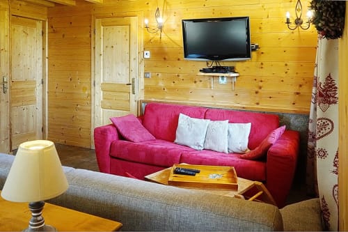 Cozy wooden chalet living room with red sofa, fireplace, TV, and mountain lodge ambiance at La Louvière