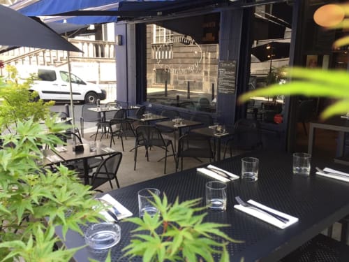 Espace repas en terrasse de La Tour Grégoire BnB à Clermont-Ferrand avec tables et chaises noires entourées de verdure
