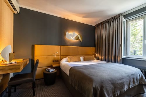 Modern hotel bedroom at Hotel Residence Europe & Spa with golden headboard, dark accent wall, and city view in Clichy, France