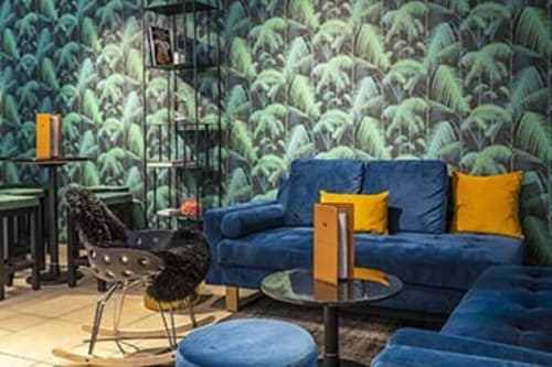 Modern lounge at Hotel Residence Europe & Spa with blue sectional sofa, tropical wallpaper, and yellow accents in Clichy
