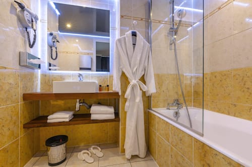 Luxurious bathroom at Hotel Residence Europe & Spa in Clichy with golden tile walls, bathtub, vanity, and white bathrobe