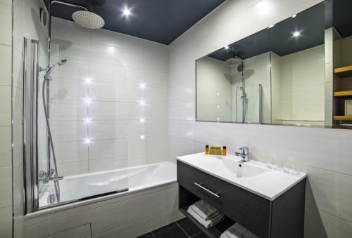 Modern bathroom in Superior Room at Hotel Residence Europe & Spa, Clichy, with white tiles, rainfall showerhead, dark vanity