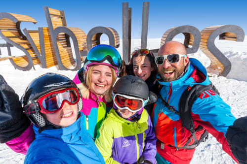 Familie van vijf personen lachend in skioutfit op het skigebied Fontcouverte-La Toussuire, Chalet La Louvière op de achtergrond