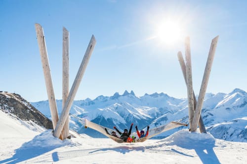 Gasten genieten van een hangmat tussen houten beeldhouwwerken in de besneeuwde Alpen van skigebied La Toussuire