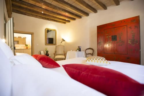Elegantes Schlafzimmer im Clos Saint Jacques B&B in Meursault mit weißer Bettwäsche, roten Kissen, sichtbaren Balken und asiatischer Kunst