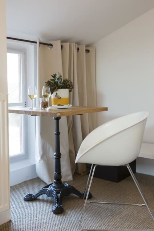 Gemütliche Ecke im Clos Saint Jacques mit Holztisch, weißem Stuhl, Weingläsern und beigefarbenen Gardinen mit Fensterblick