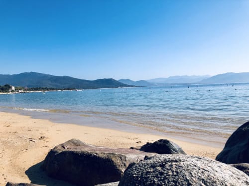Plage pittoresque de Villas Marincelu aux eaux turquoise, sable fin, rochers et montagnes à Porto Pollo, Corse