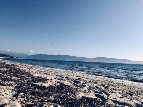 Playa rocosa en Villas Marincelu con mar Mediterráneo azul turquesa y montañas, Porto Pollo, Córcega
