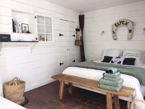 Gemütliches Schlafzimmer im Les Filles du Bord de Mer mit weißen Schindeldächern, Holzbank, gestapelten Handtüchern und Hafenblick