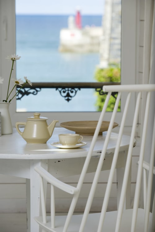 Elegante Teezeremonie am Meer mit cremefarbeener Teekanne und Tasse mit Blick auf den Hafen des Cottage Les Filles du Bord de Mer