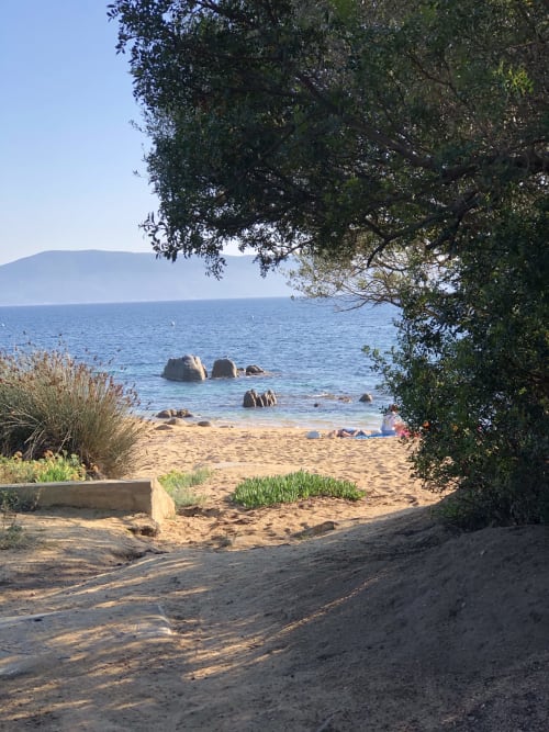 Scenic beach view at Villas Marincelu with sandy shore, rocky outcrops, and mountains across the water in Serra di Ferro
