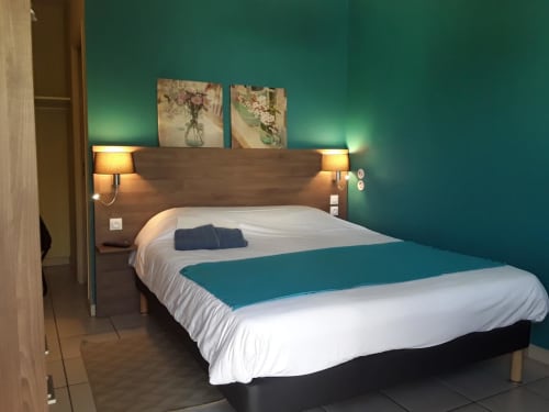 Chambre moderne du Relais Motel de Maisonnay aux murs bleu-vert, literie blanche et tête de lit en bois foncé avec lampes